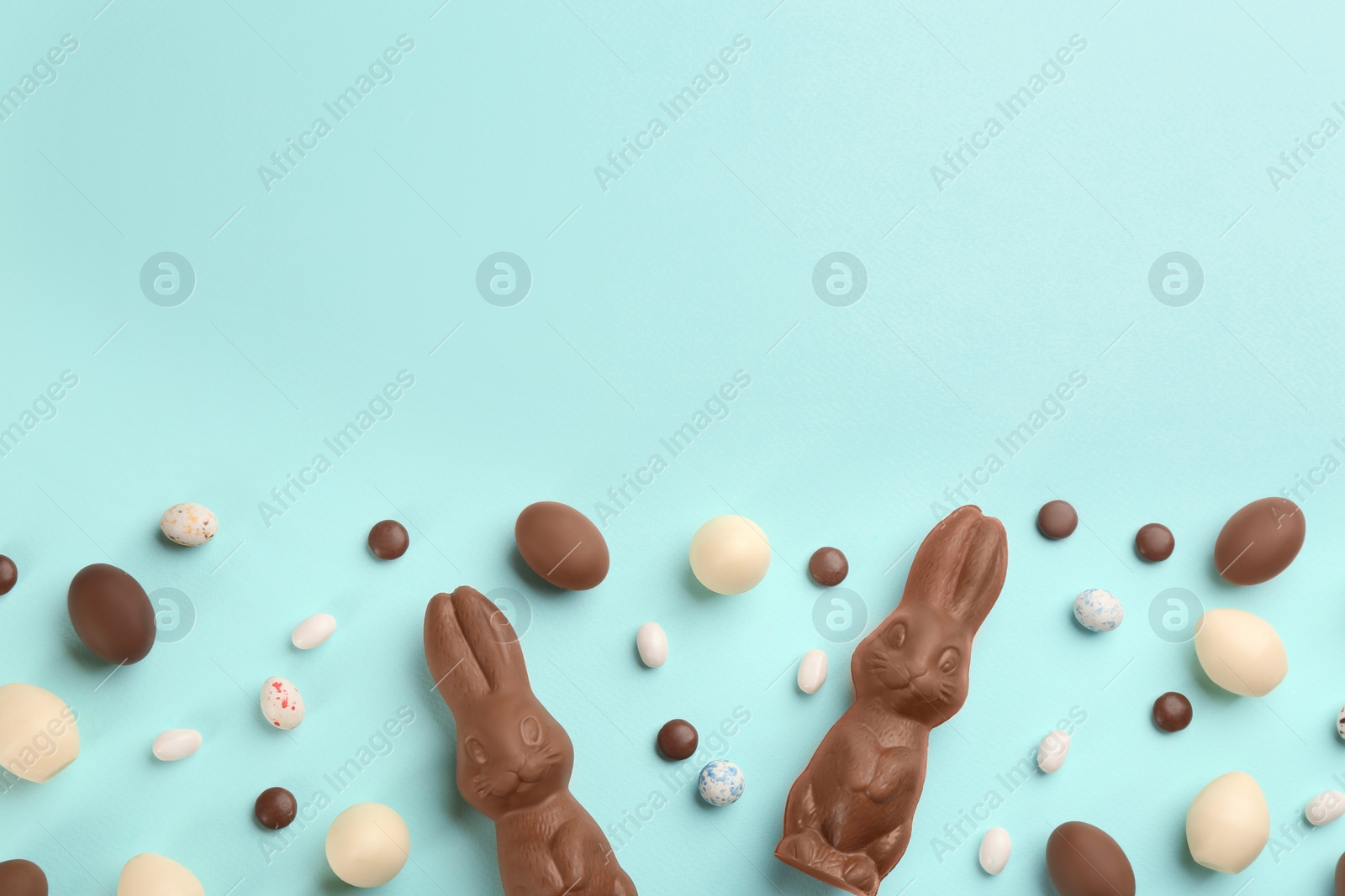 Photo of Flat lay composition with chocolate Easter bunnies, eggs and candies on light blue background. Space for text