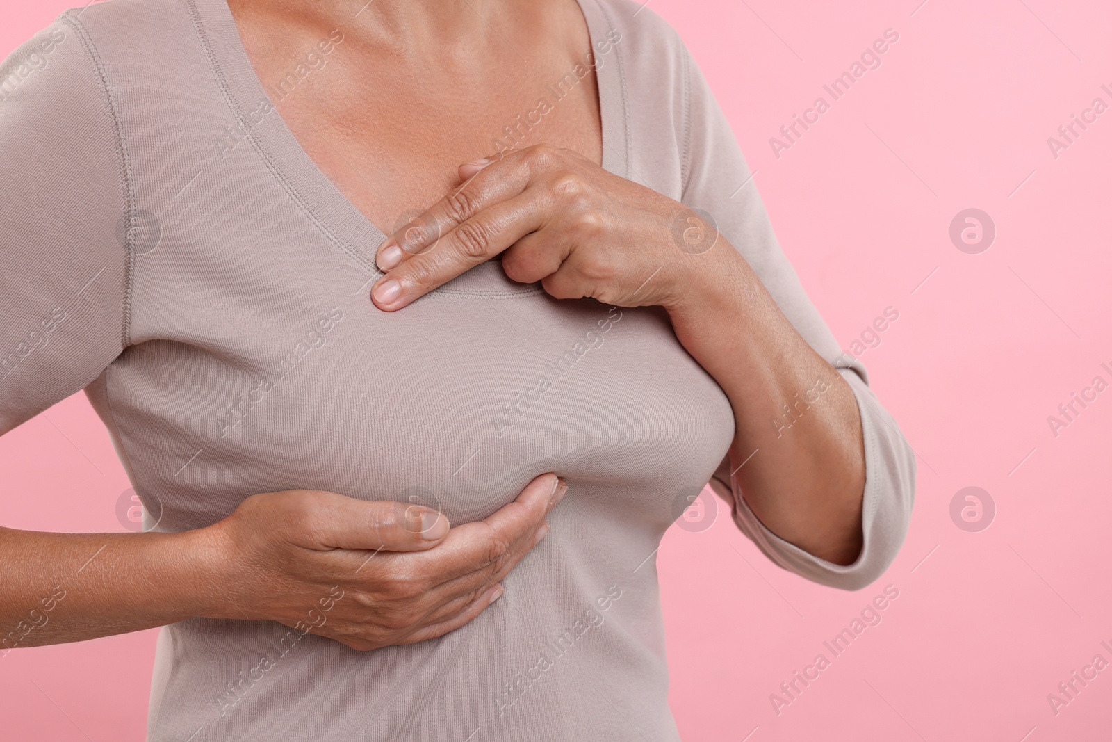 Photo of Woman doing breast self-examination on pink background, closeup