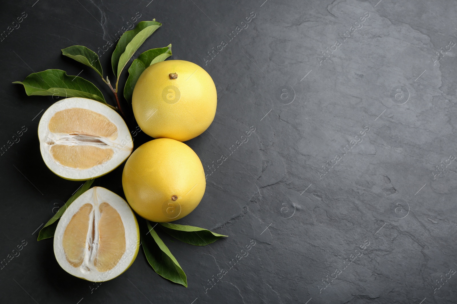 Photo of Fresh cut and whole pomelo fruits on black slate table, flat lay. Space for text