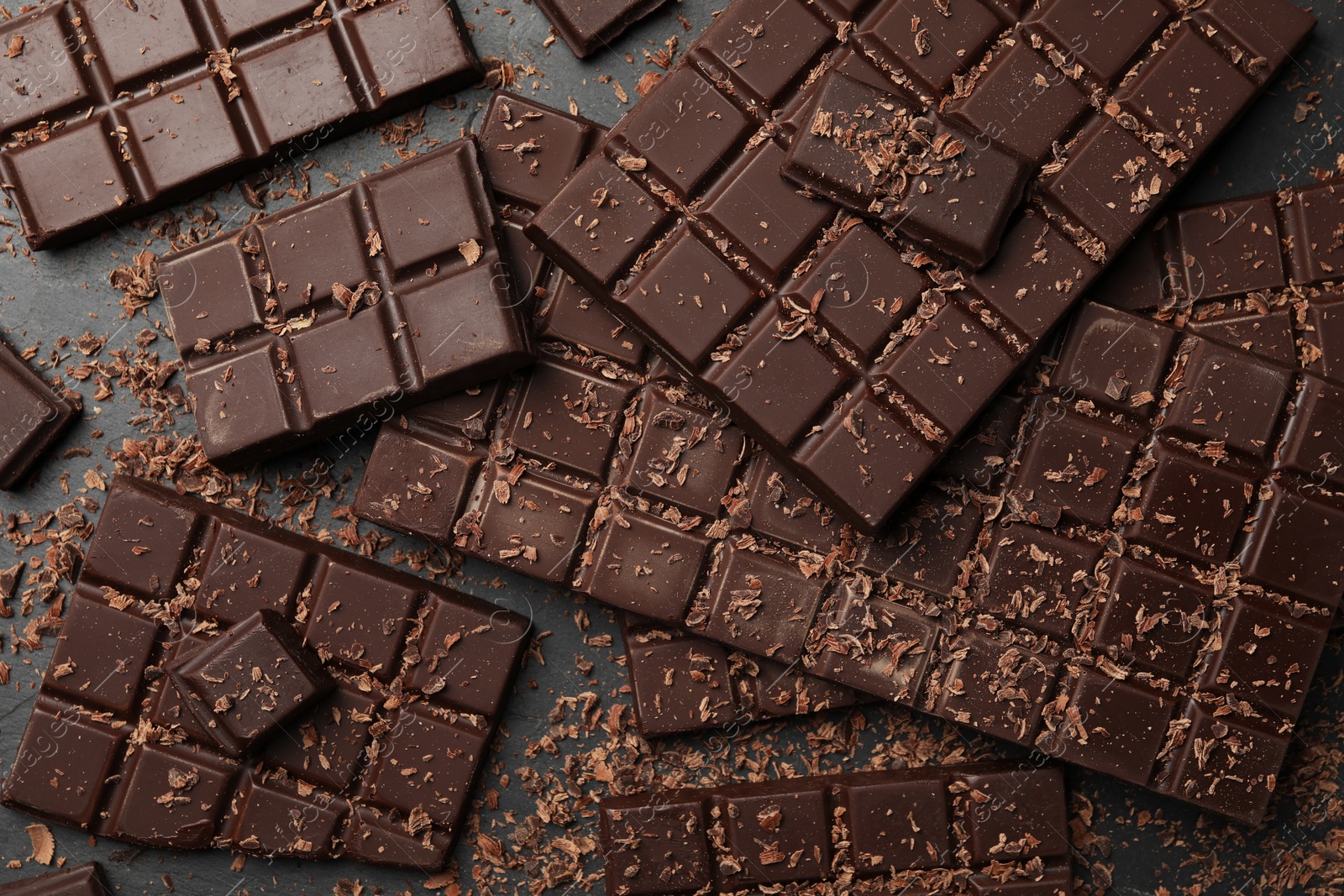 Photo of Pieces and shavings of tasty chocolate bars on grey table, flat lay