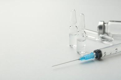 Glass ampoules with liquid and syringe on white background, closeup. Space for text