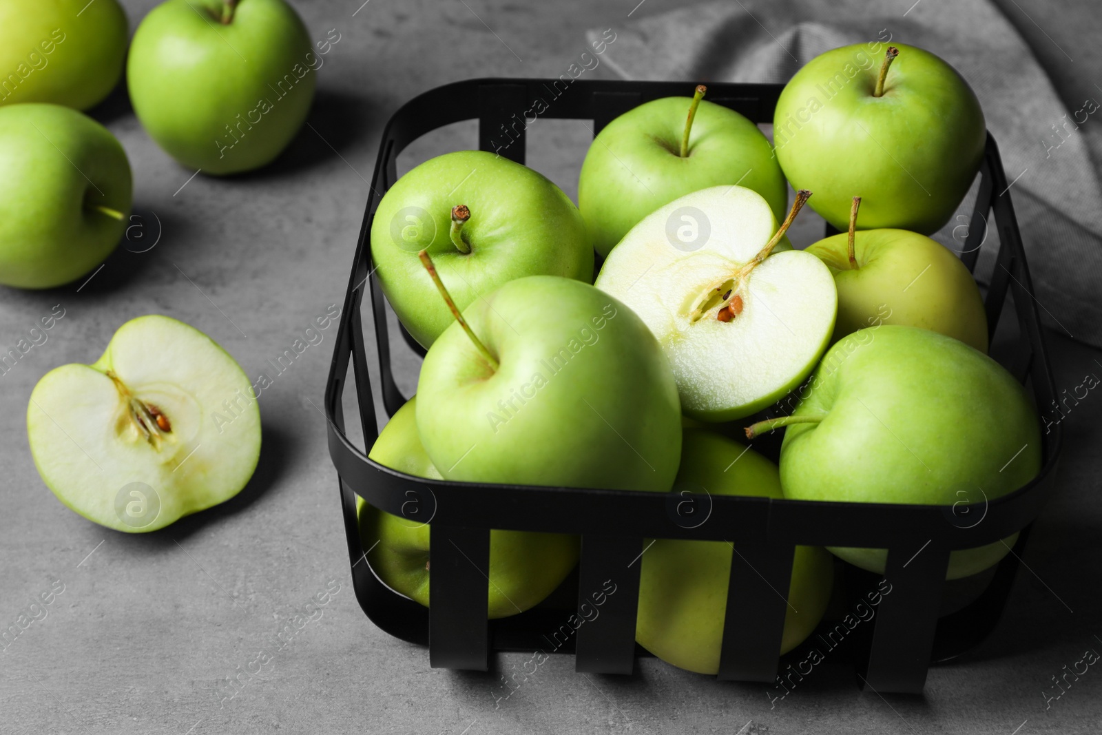 Photo of Black metal container full of apples on grey table, closeup