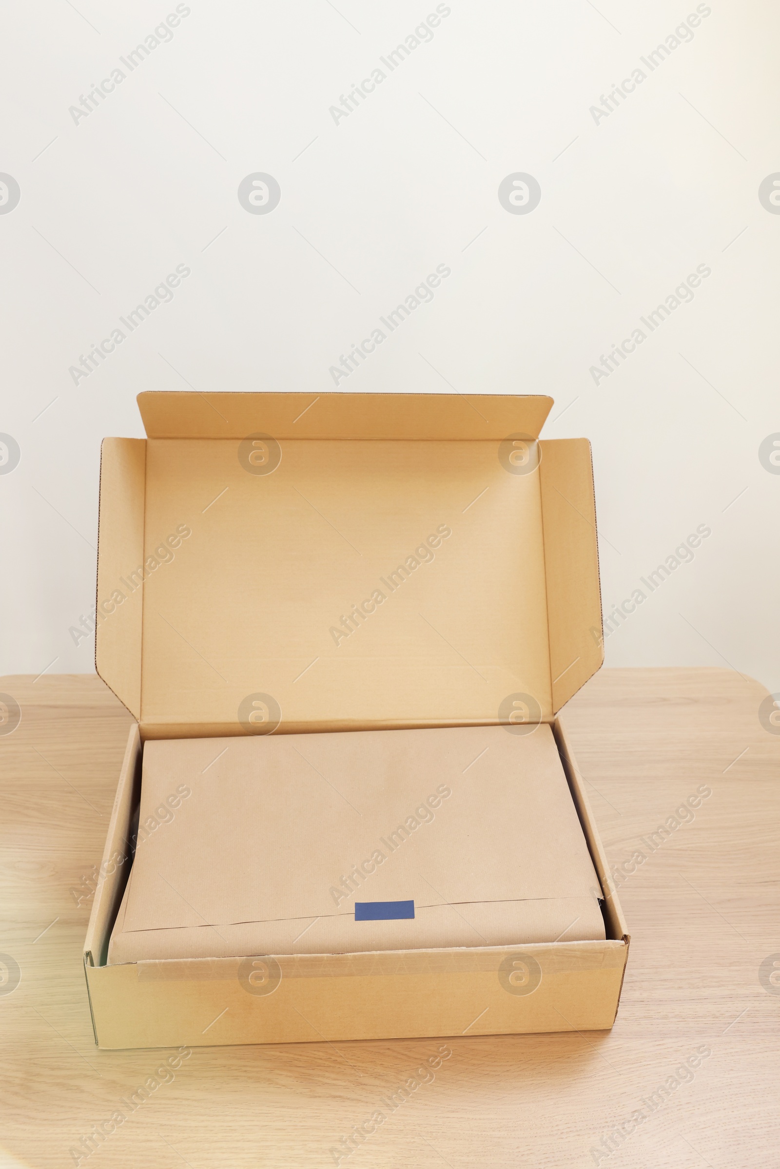 Photo of Open cardboard box with item wrapped in kraft paper on wooden table. Delivery service