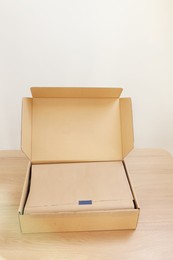 Photo of Open cardboard box with item wrapped in kraft paper on wooden table. Delivery service