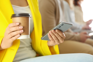 Woman with cup of coffee using smartphone, closeup