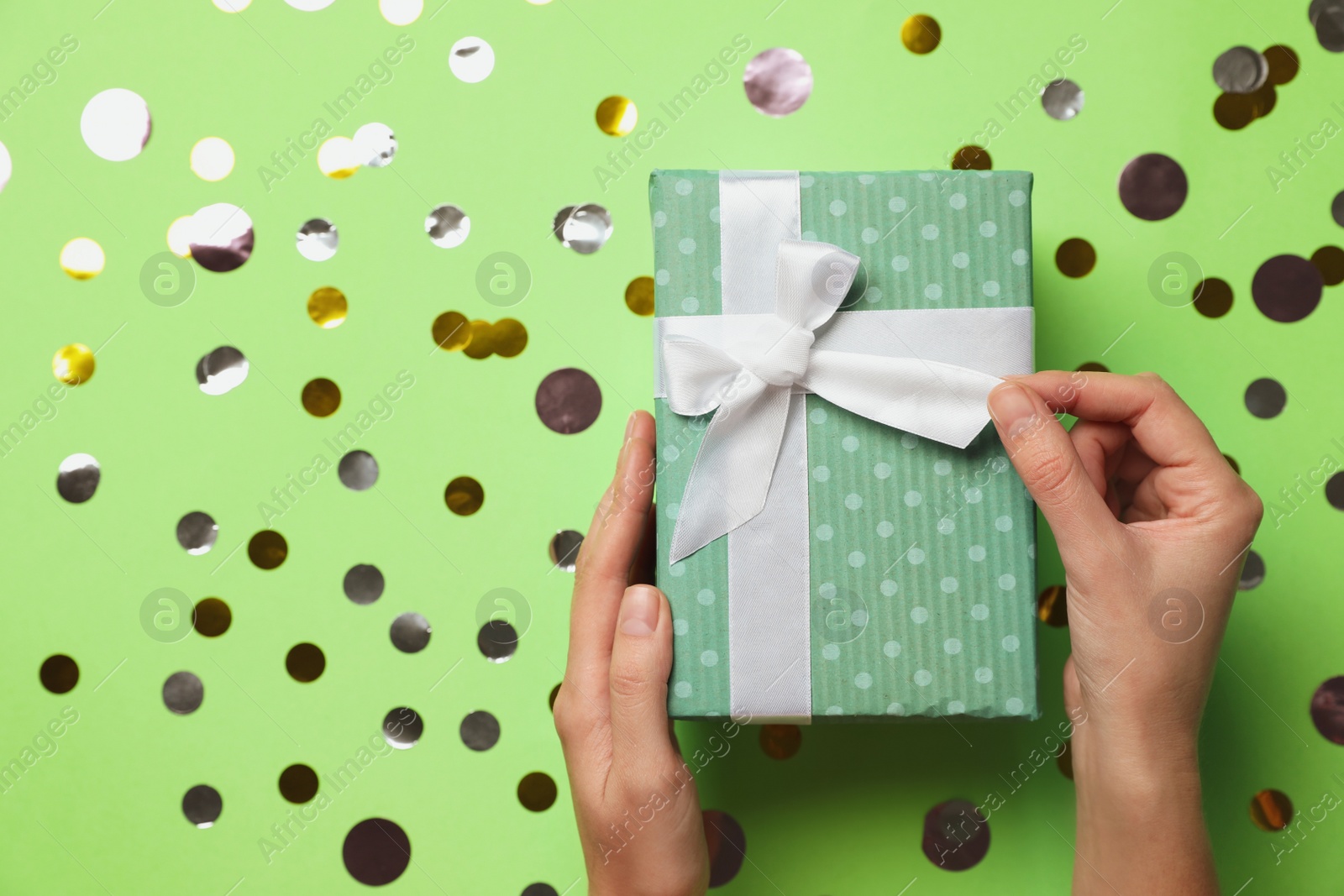 Photo of Woman holding Christmas gift on green background with silver confetti, top view. Space for text