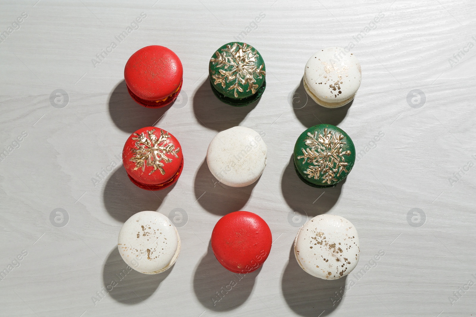 Photo of Different decorated Christmas macarons on wooden table, flat lay
