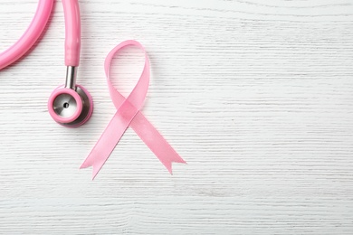 Photo of Pink ribbon and stethoscope on wooden background, top view with space for text. Breast cancer concept