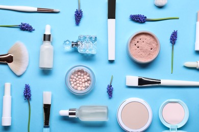 Flat lay composition with different makeup products and beautiful spring flowers on light blue background