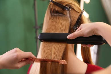 Photo of Stylist straightening woman's hair with flat iron in salon