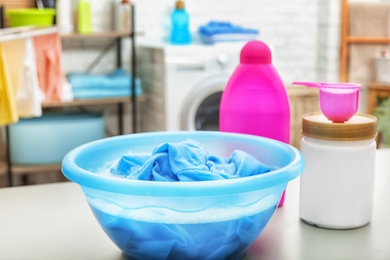 Photo of Color clothes with foam in basin and detergents on table in bathroom