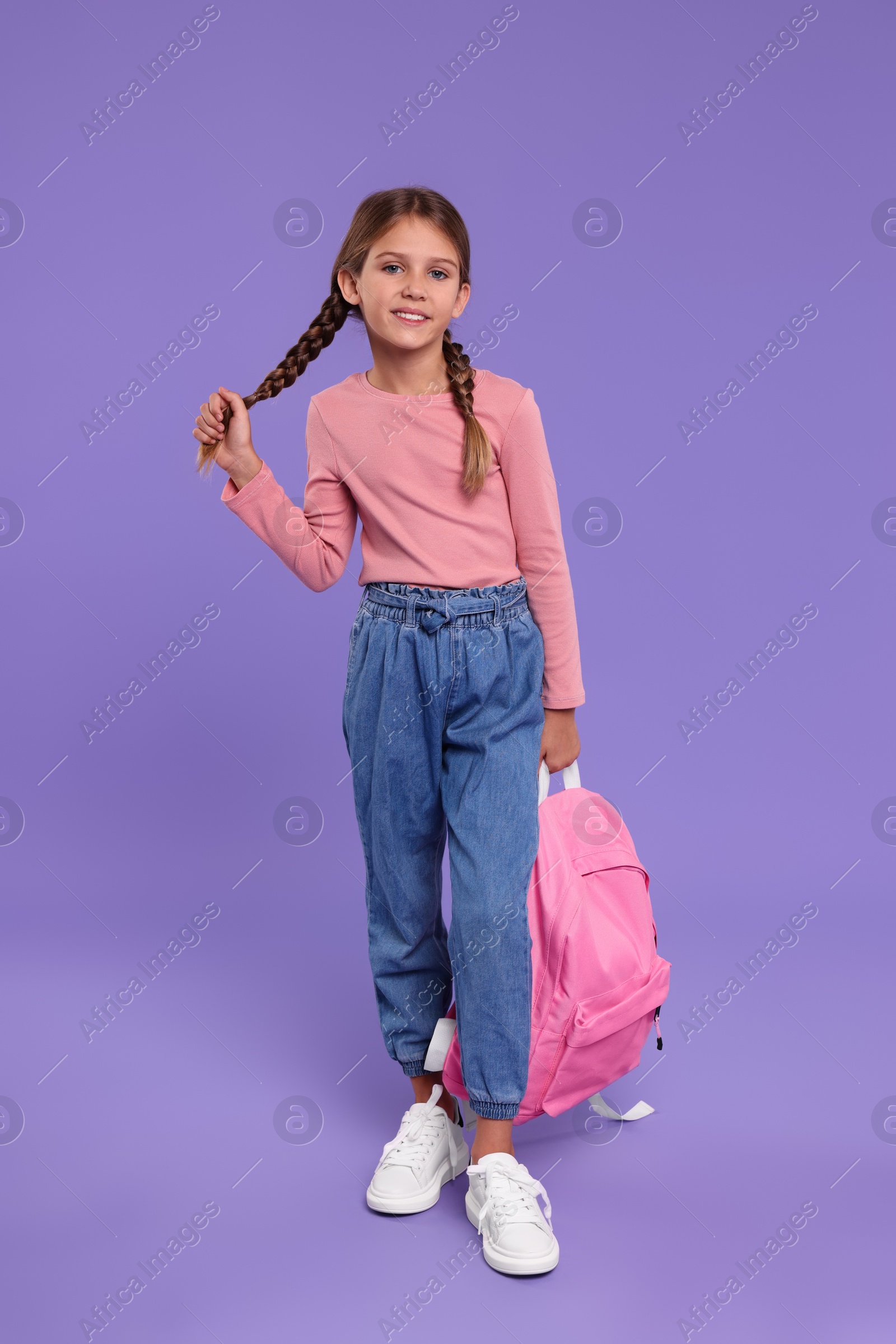 Photo of Happy schoolgirl with backpack on violet background