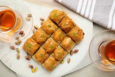 Delicious sweet baklava with pistachios and hot tea on light grey table, flat lay