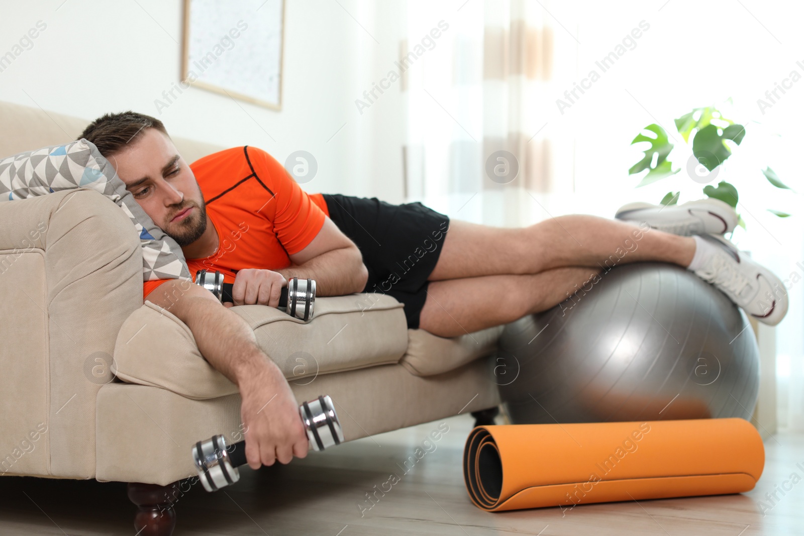 Photo of Lazy young man with sport equipment on sofa at home