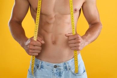 Photo of Shirtless man with slim body and measuring tape on yellow background, closeup