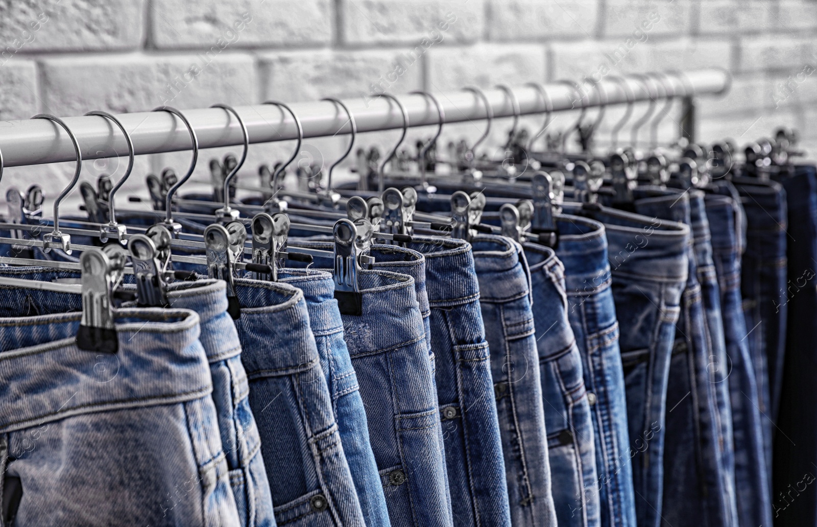 Photo of Rack with stylish jeans near brick wall, closeup