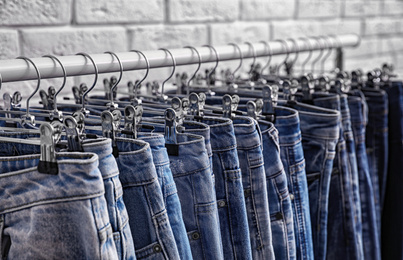 Rack with stylish jeans near brick wall, closeup