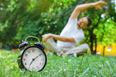 Photo of Man doing morning exercise in park, focus on alarm clock