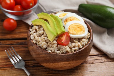 Photo of Tasty boiled oatmeal with egg, avocado and tomato served on wooden table, closeup