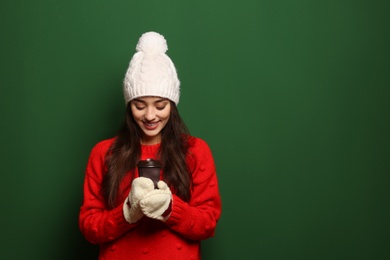 Young woman in sweater with cup of hot coffee on color background, space for text. Winter season