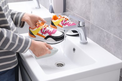 Photo of Woman washing stylish sneakers with brush in sink, closeup