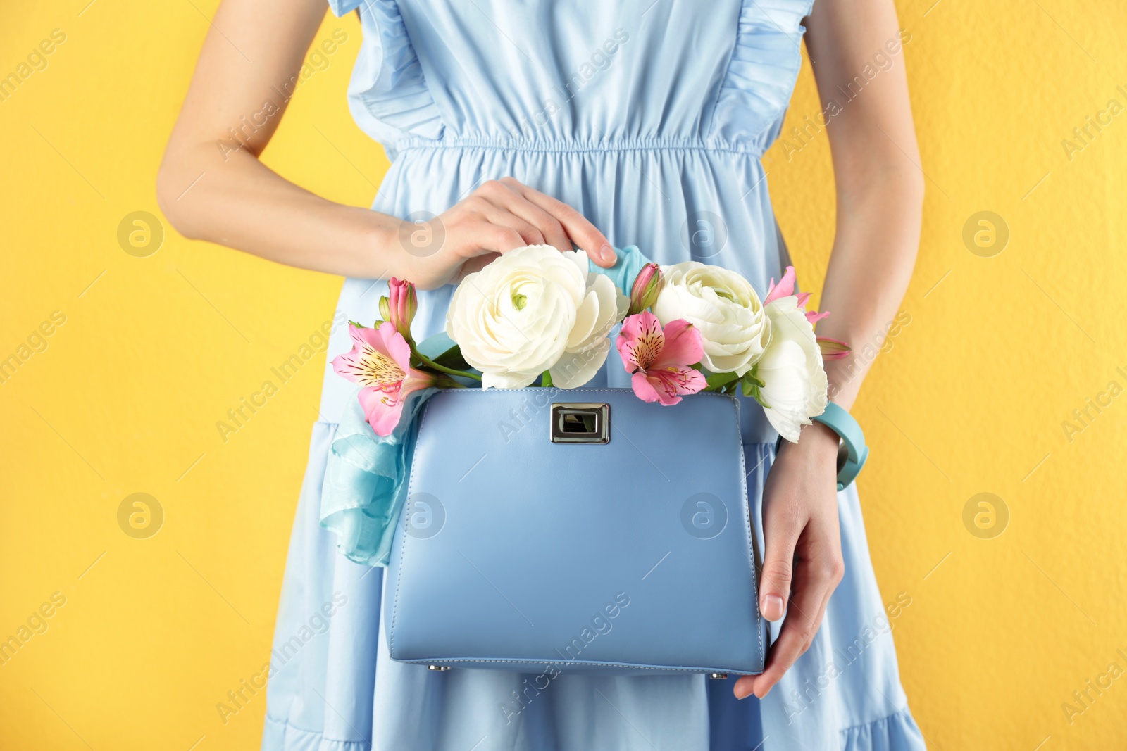 Photo of Woman holding elegant handbag with spring flowers on yellow background, closeup