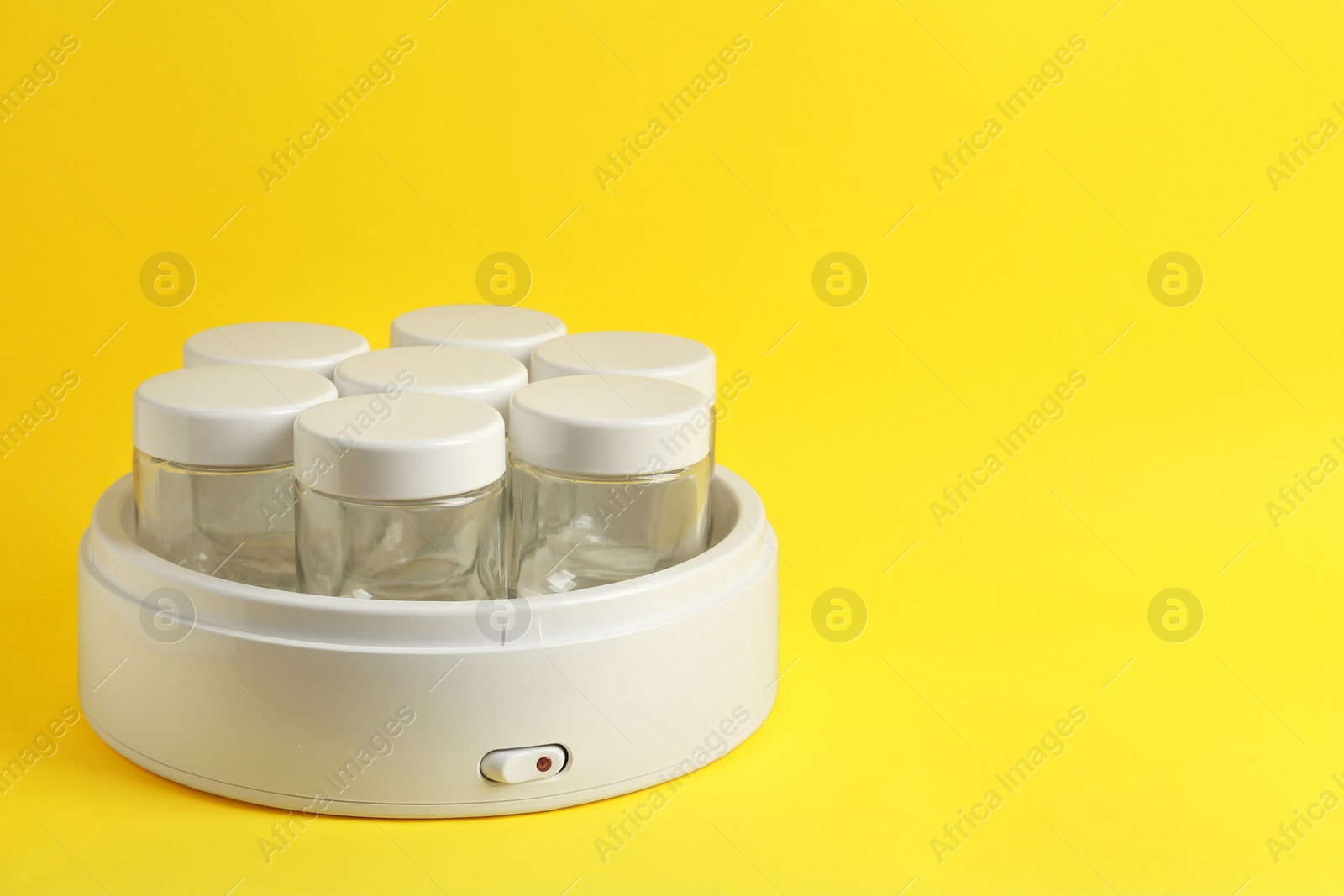 Photo of Modern yogurt maker with empty jars on yellow background, space for text