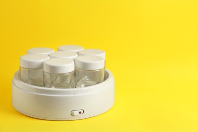 Photo of Modern yogurt maker with empty jars on yellow background, space for text