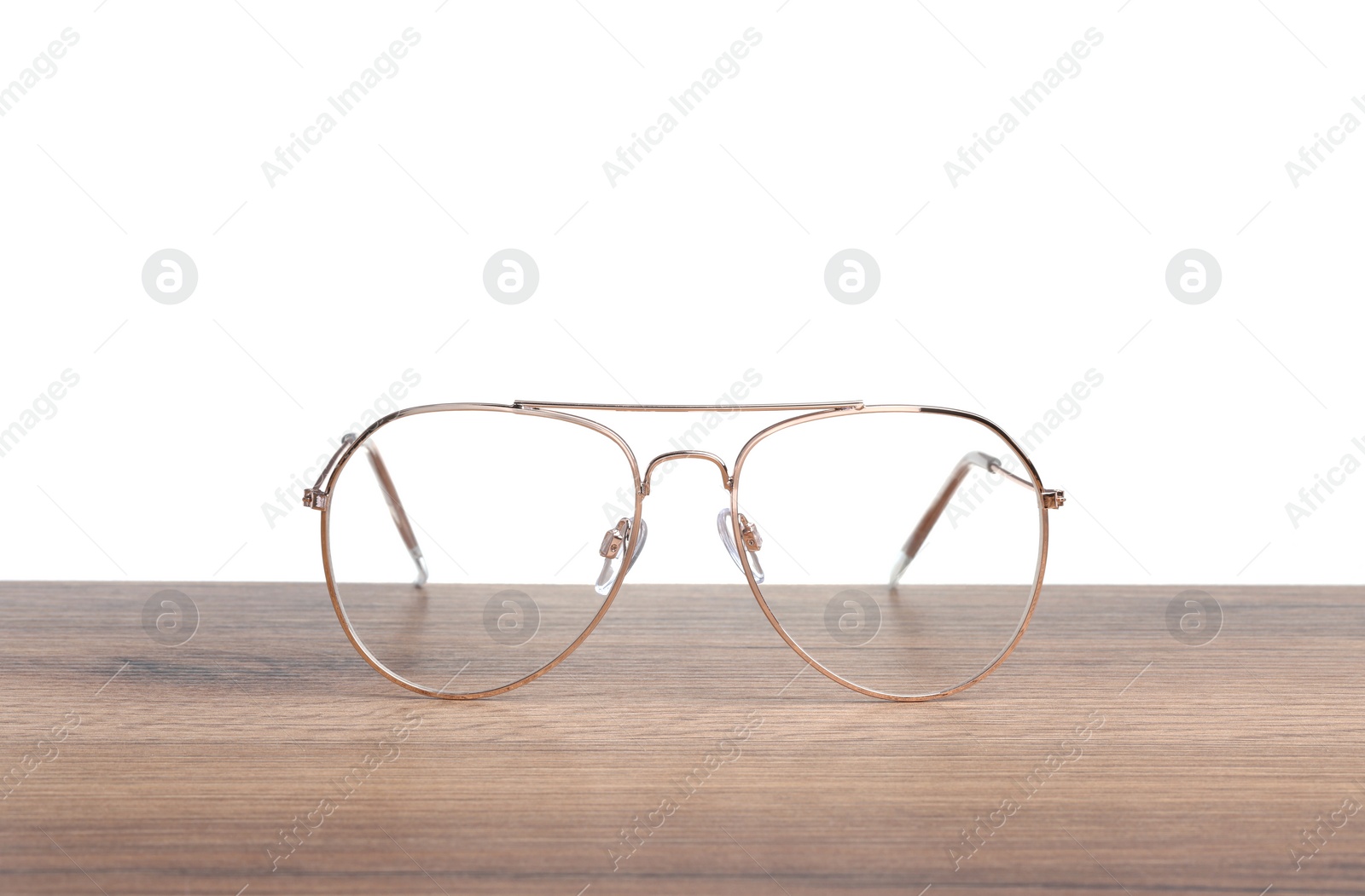 Photo of Stylish glasses with metal frame on wooden table against white background