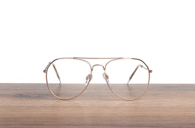 Photo of Stylish glasses with metal frame on wooden table against white background