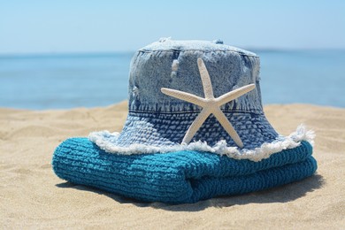 Photo of Stylish denim hat, towel and starfish on sand near sea. Beach accessories