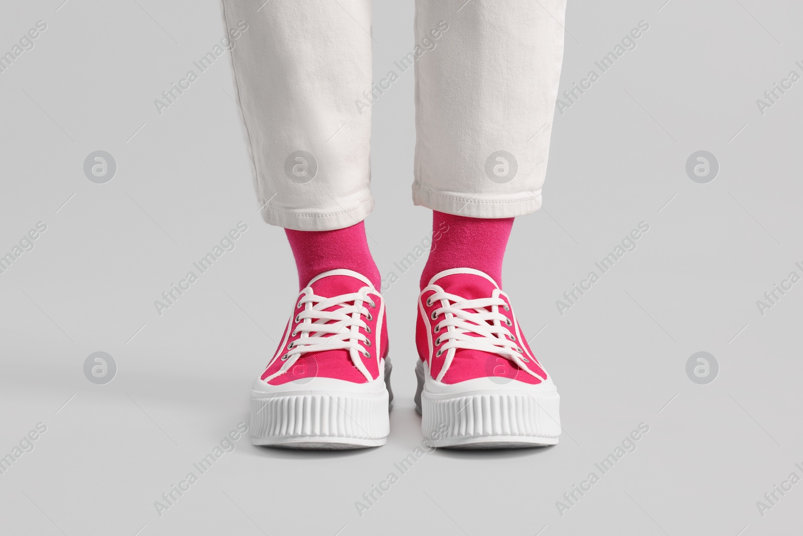 Photo of Woman in stylish bright pink socks, sneakers and pants on light grey background, closeup