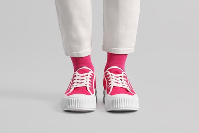 Woman in stylish bright pink socks, sneakers and pants on light grey background, closeup