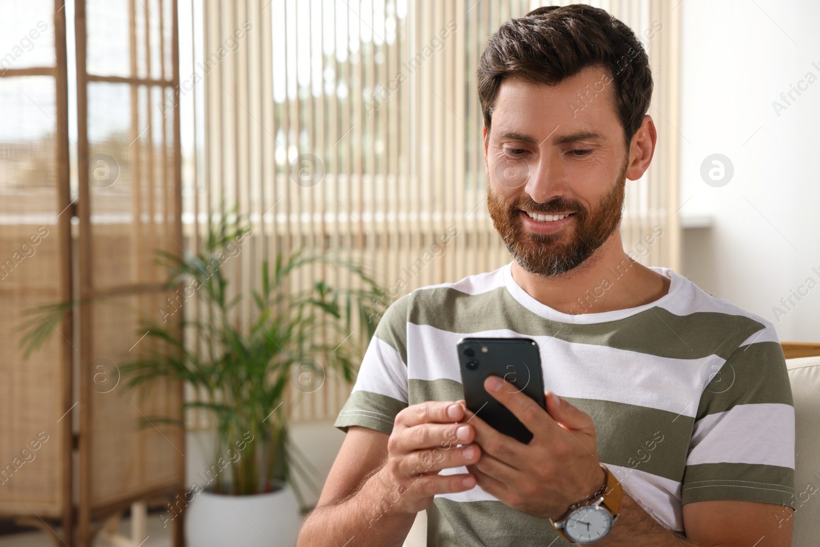 Photo of Handsome man using smartphone at home, space for text