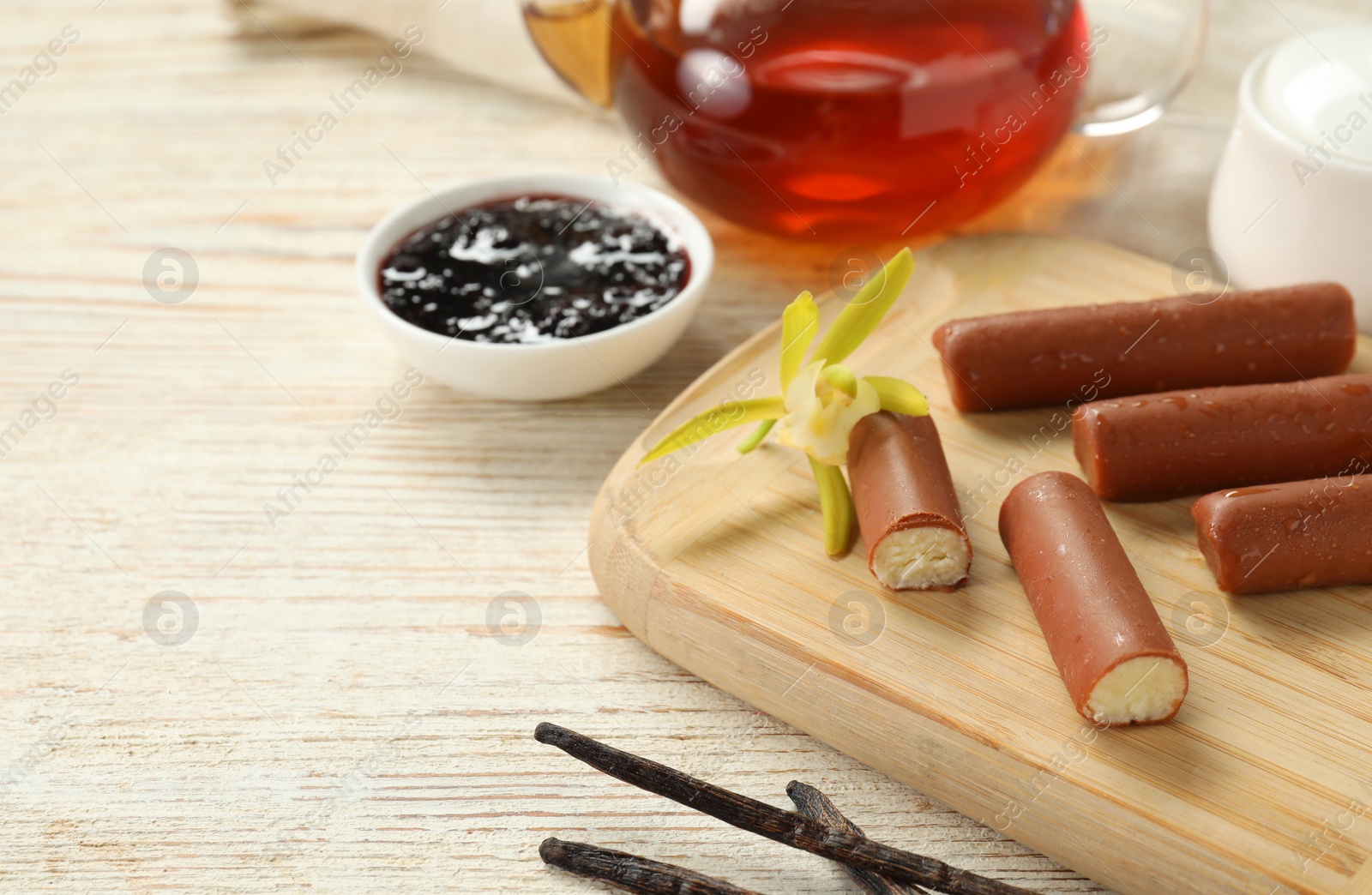 Photo of Glazed curd cheese bars, vanilla pods and tea on white wooden table, closeup. Space for text