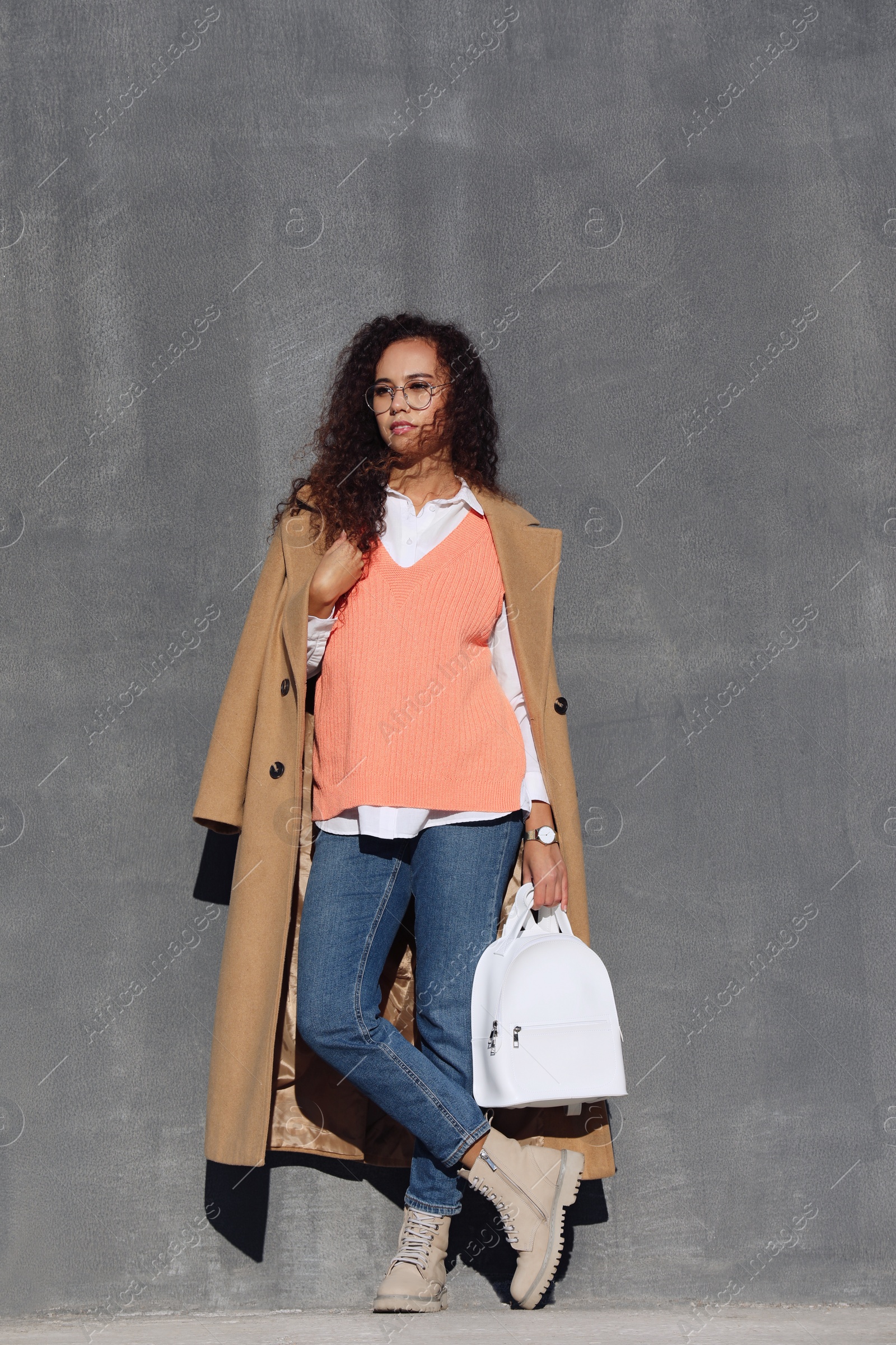 Photo of Full length portrait of beautiful African-American woman with stylish white backpack near grey wall outdoors