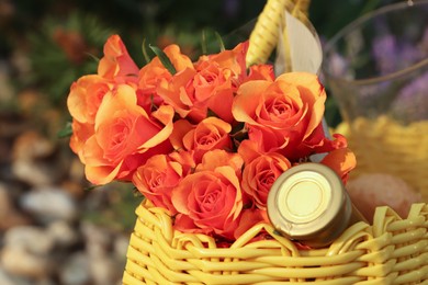 Photo of Yellow wicker bag with beautiful roses and bottle of wine outdoors