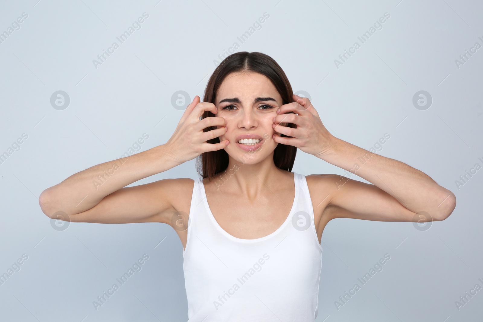 Photo of Young woman scratching face on light background. Annoying itch