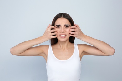 Young woman scratching face on light background. Annoying itch