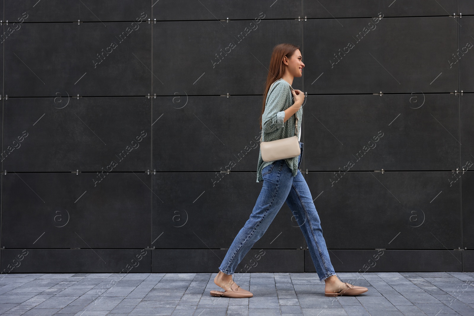 Photo of Young woman in casual clothes walking near grey wall outdoors, space for text