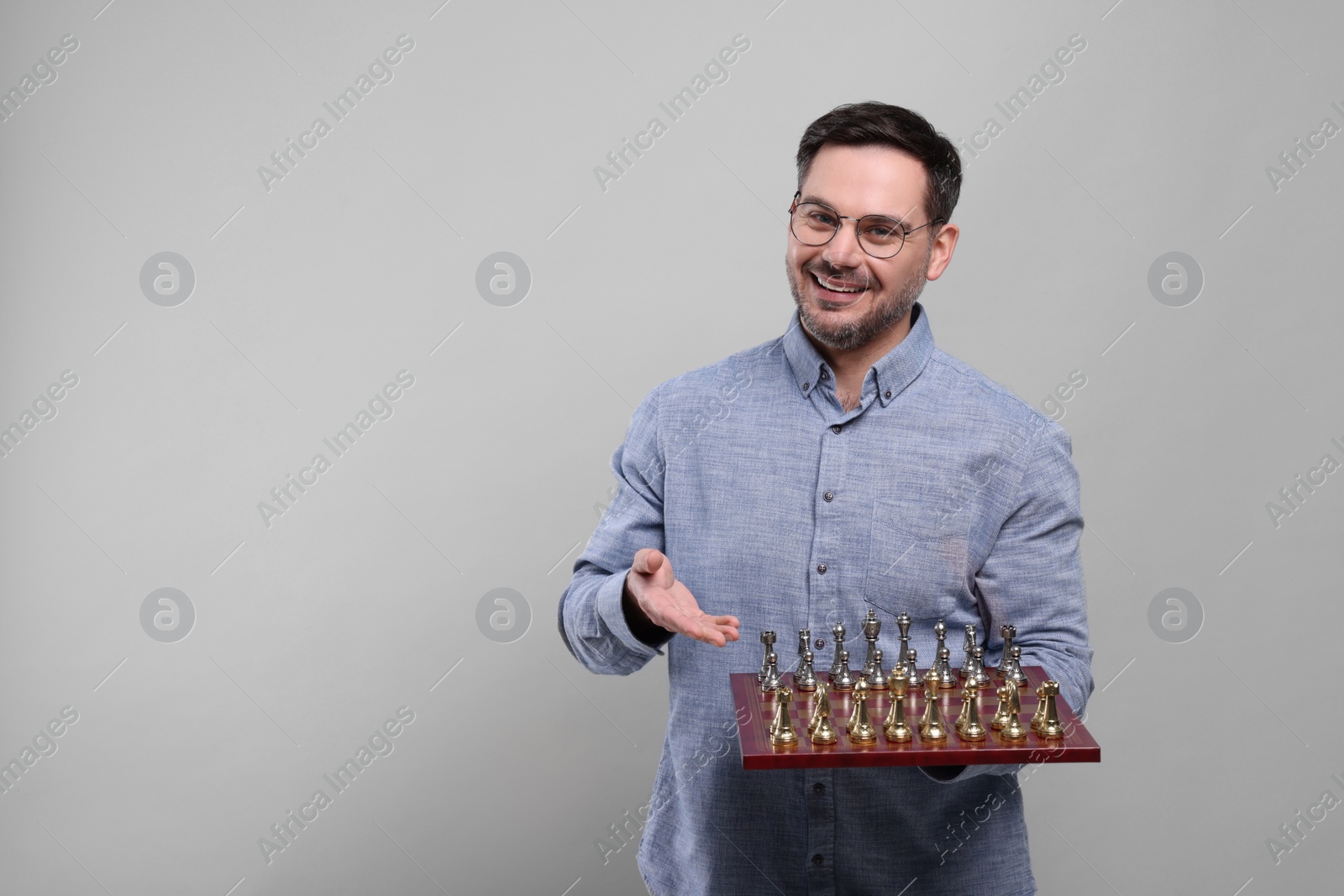 Photo of Smiling man showing chessboard with game pieces on light grey background, space for text