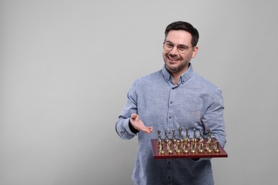 Photo of Smiling man showing chessboard with game pieces on light grey background, space for text