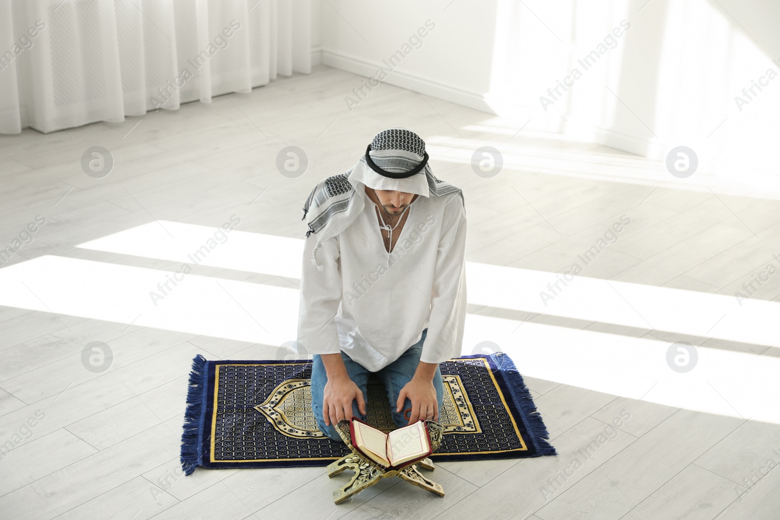 Photo of Muslim man with Koran praying on rug indoors