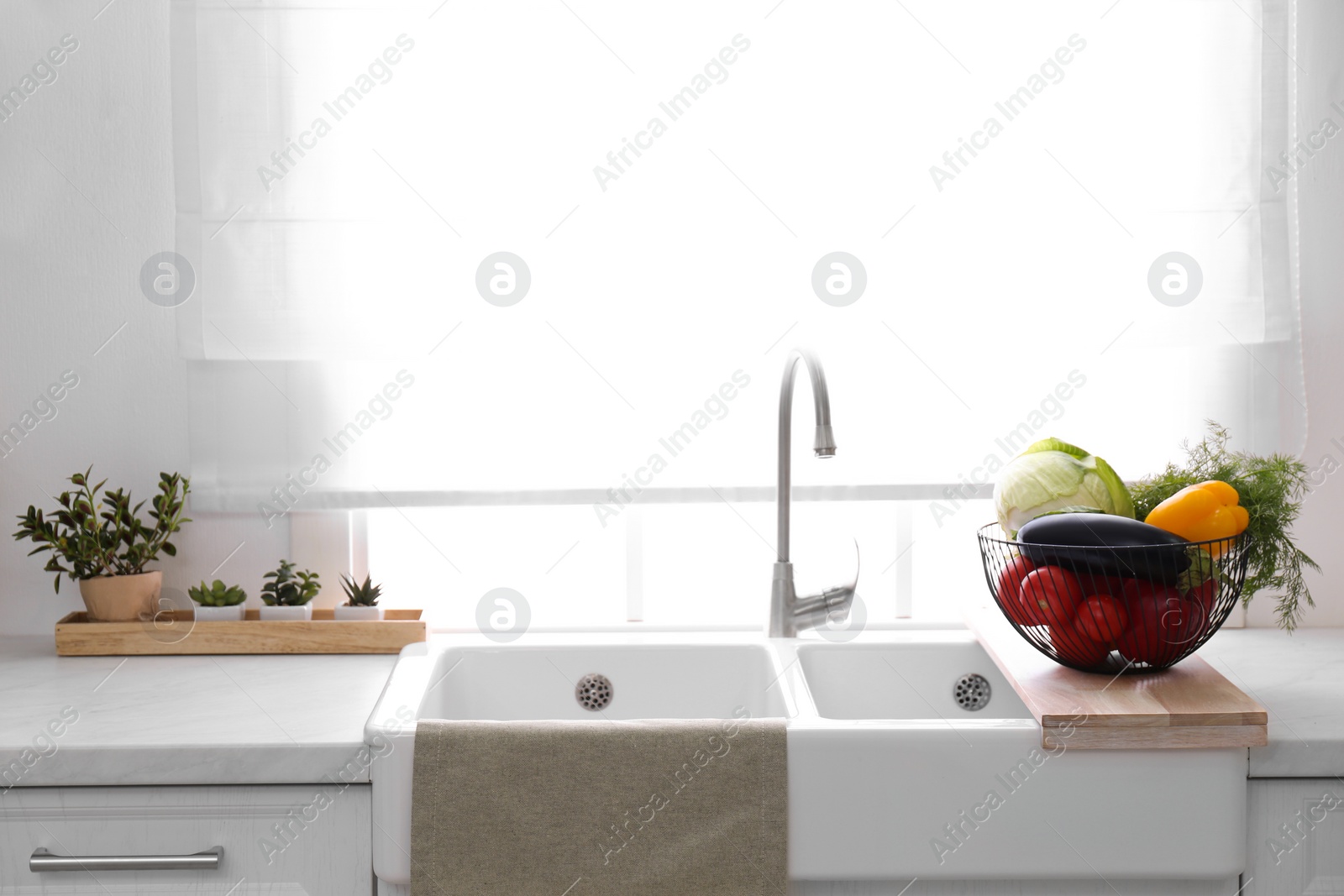 Photo of Basket full of different vegetables on wooden board in modern kitchen