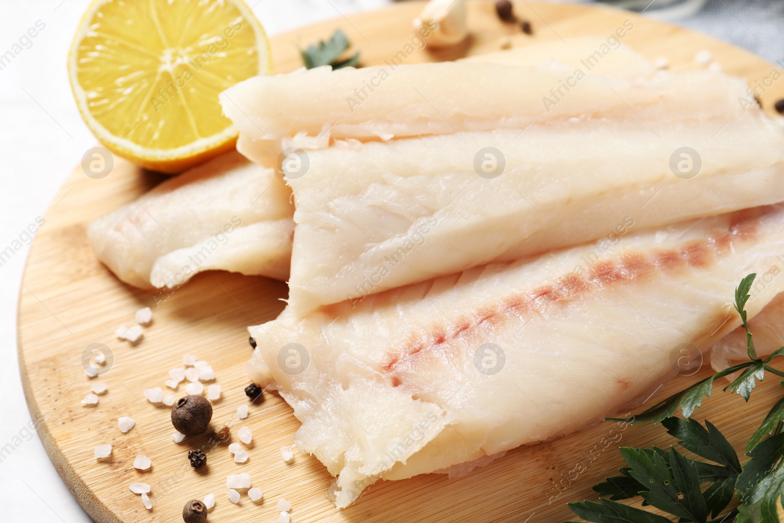 Photo of Pieces of raw cod fish, spices, parsley and lemon on table, closeup