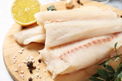Photo of Pieces of raw cod fish, spices, parsley and lemon on table, closeup