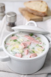 Delicious cold summer soup (okroshka) with boiled sausage in pot on table