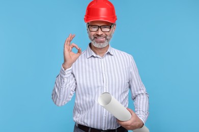 Architect in hard hat holding draft and showing ok gesture on light blue background