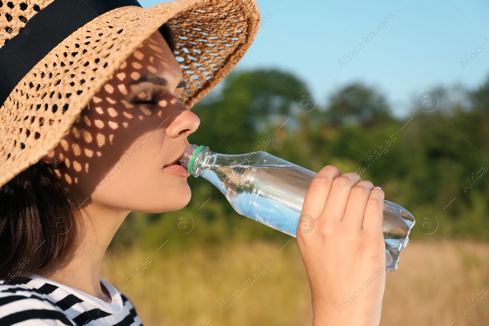 Photo of Young woman in straw hat drinking water outdoors on hot summer day. Refreshing drink