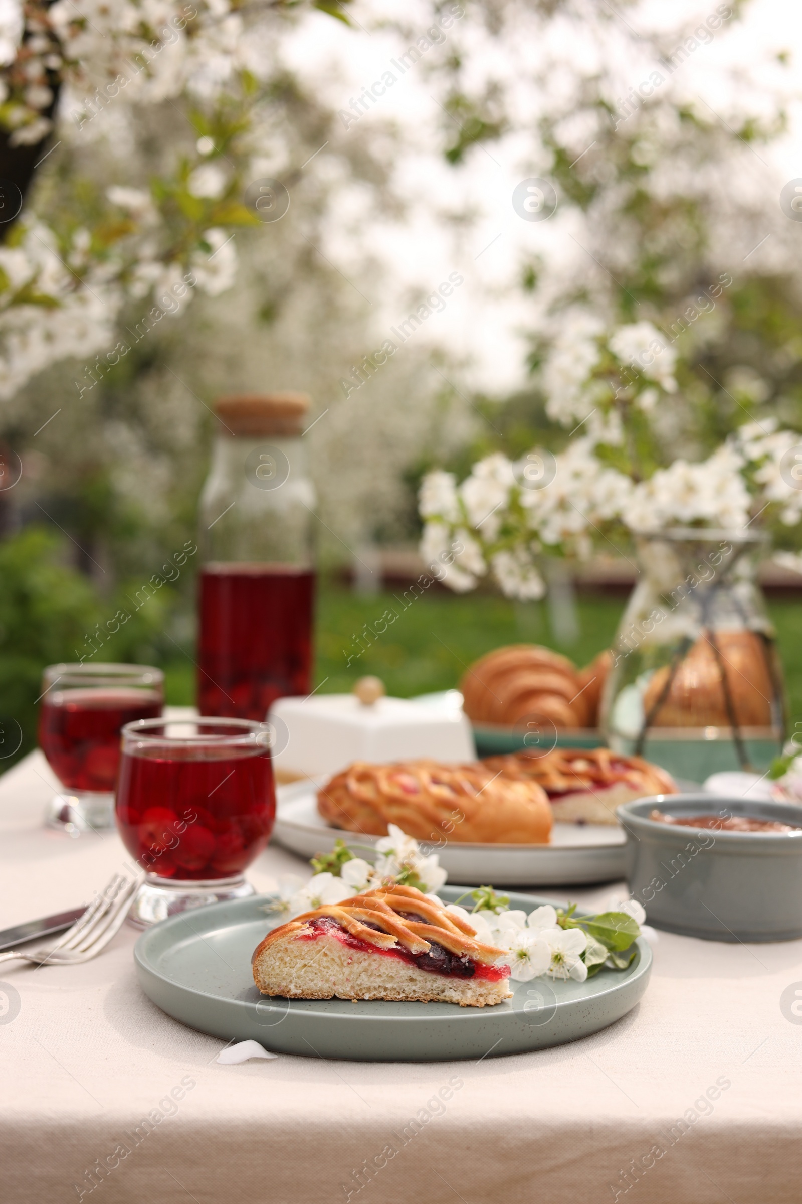 Photo of Stylish table setting with beautiful spring flowers, fruit drink and pie in garden